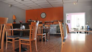 A restaurant with wooden chairs and tables, a clock on the wall, and a bar area with bottles and glasses.