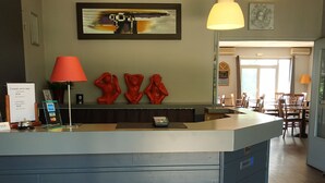 A reception desk with a blue counter, overhead pendant lights, and a framed abstract painting above. - Hotel Restaurant du Lac (Boe)