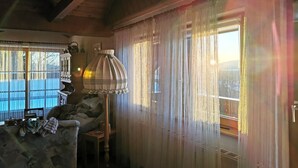 A cozy room with a wooden ceiling, a lamp, a couch, and a window with sheer curtains. - Ferienhaus Haidweg (Haidmuhle)