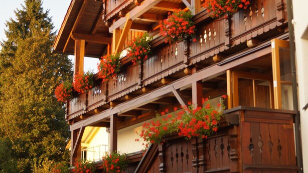 A multi-story wooden building with balconies adorned with red flowers. - Ferienhaus Haidweg (Haidmuhle)