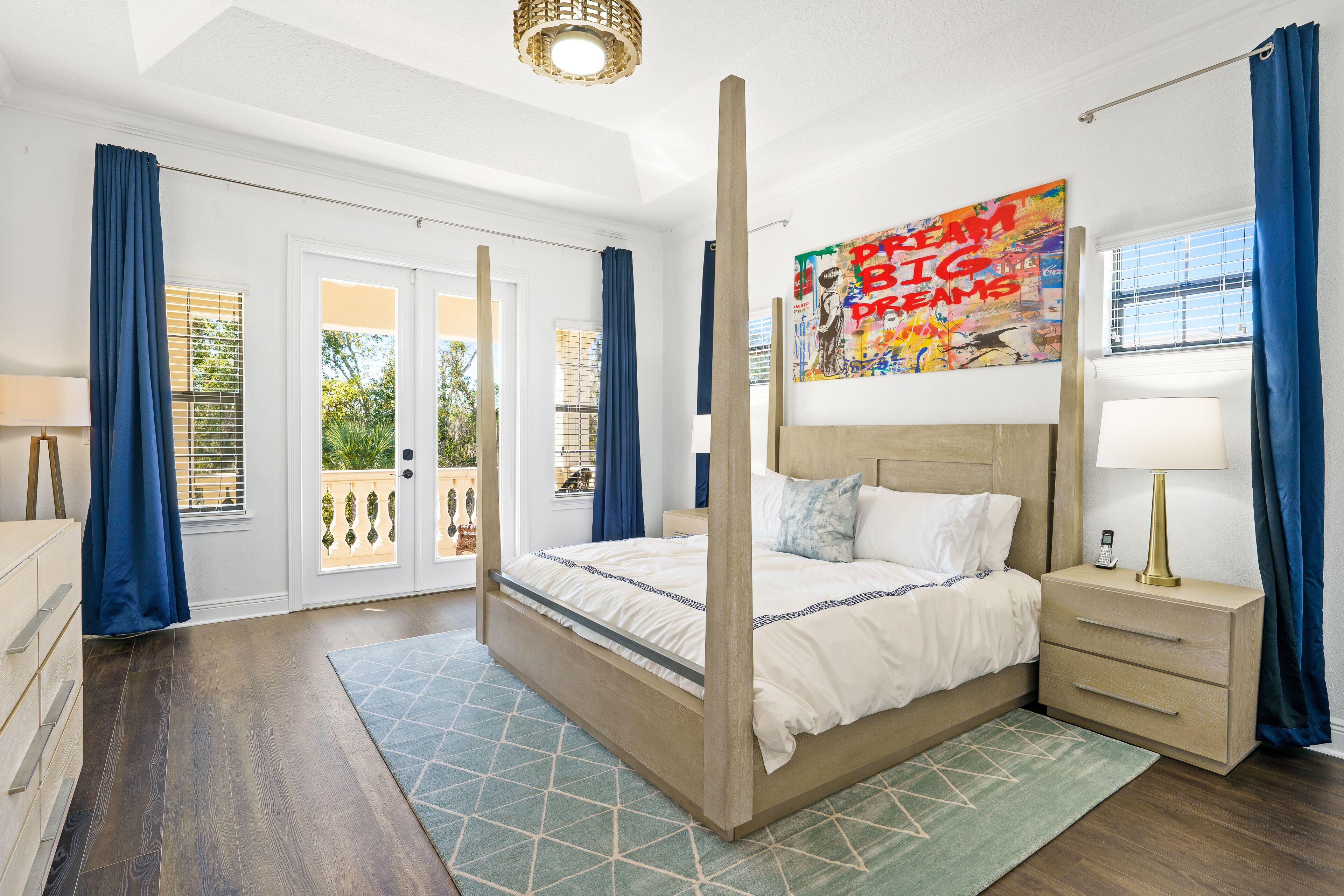 A four-poster bed with a wooden frame, a bedside table with a lamp, and a colorful abstract painting on the wall.