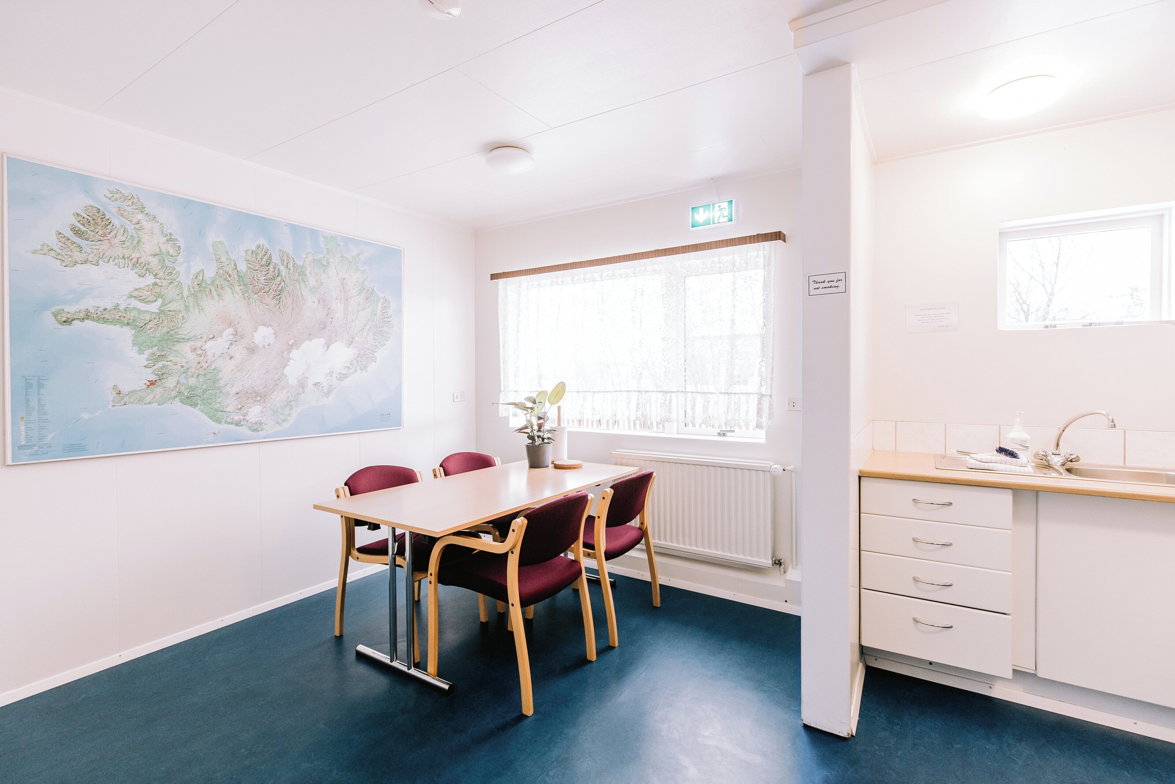 A room with a large map on the wall, a table with chairs, a window with blinds, and a kitchenette area.