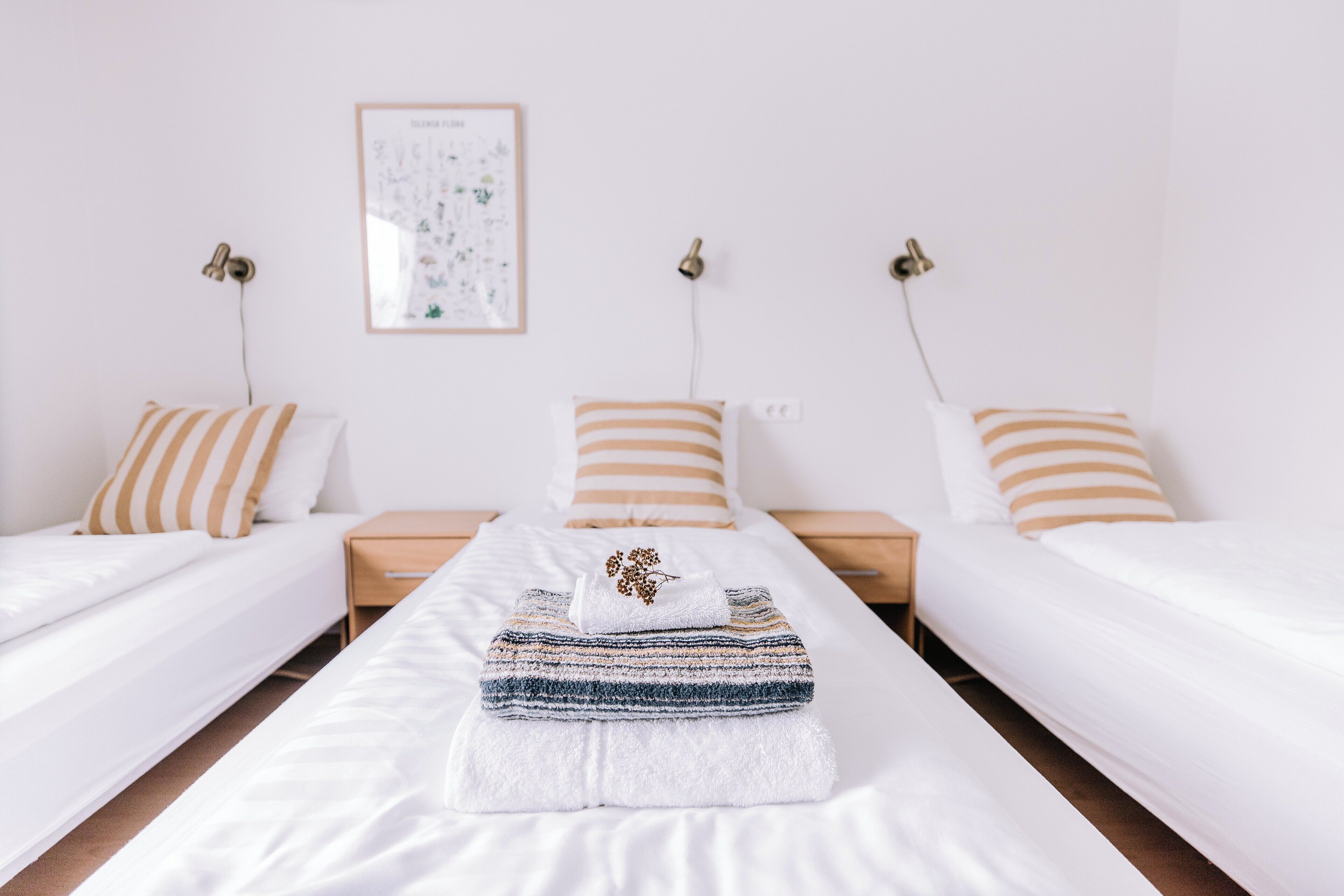 A hotel room with two single beds, a large bed with a striped blanket, and a framed botanical print on the wall.