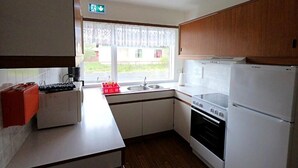 A compact kitchen with a stove, oven, and refrigerator. There is a window with a view of a building outside. - Eldá Guesthouse (Myvatn)