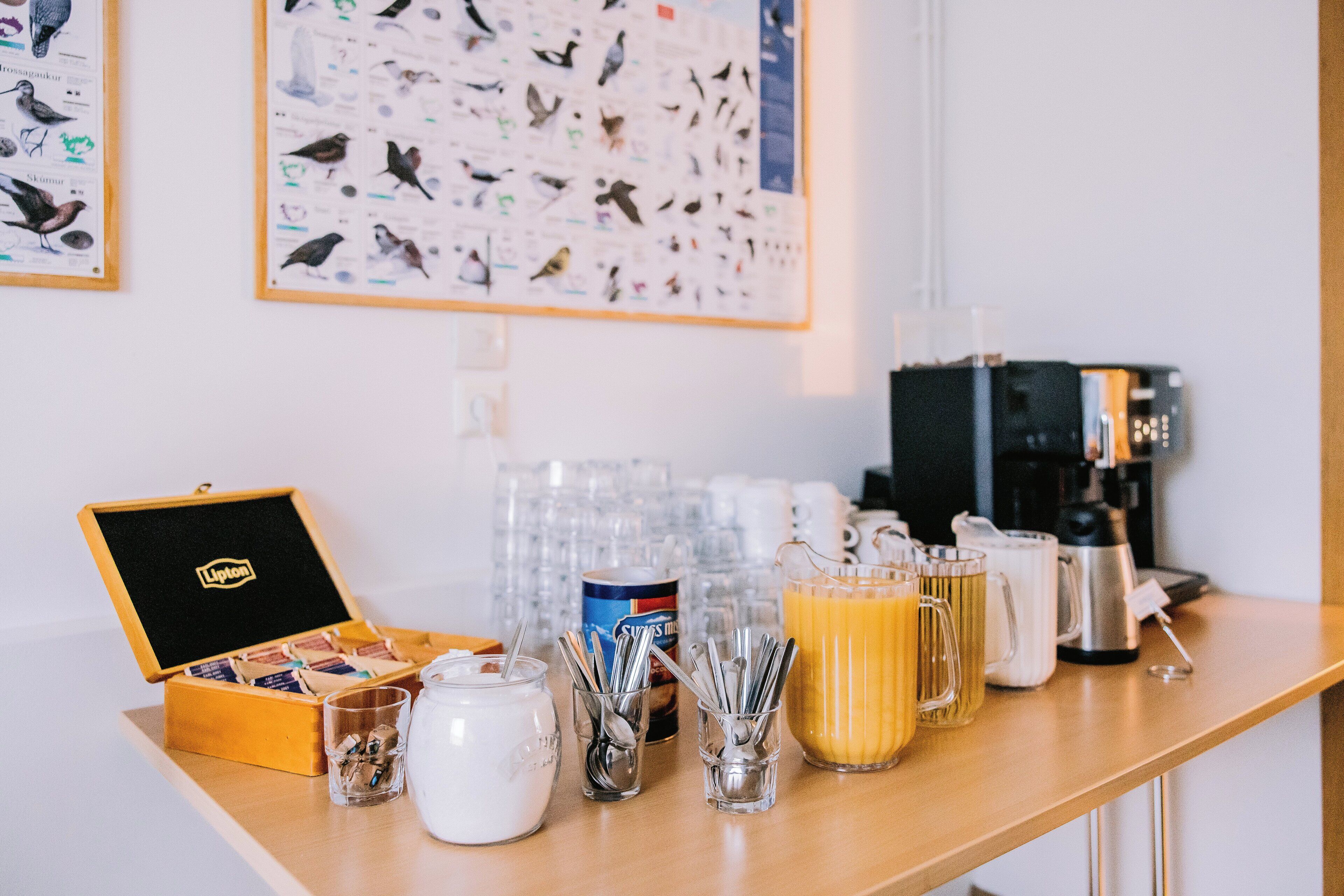 A breakfast bar with a coffee maker, a jar of sugar, a box of tea bags, and a bird-themed wall hanging.