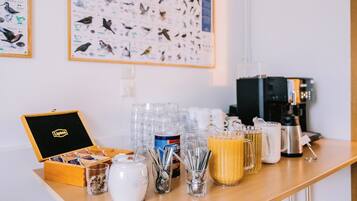 A breakfast bar with a coffee maker, a jar of sugar, a box of tea bags, and a bird-themed wall hanging.
