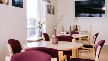 A dining area with round tables and chairs, a vase with dried plants, and artwork on the walls.