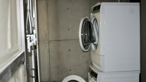 Pequeña lavandería con lavadora y secadora apiladas, un inodoro y una puerta metálica.