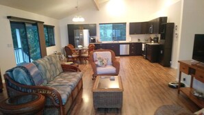 A spacious living area with a sofa, chairs, and a coffee table. A kitchen with dark cabinets and appliances is visible in the background. - Big Private Mt. Home Minutes to Volcanos National Park
Myra's Blue Hawaii House  (Ocean View)