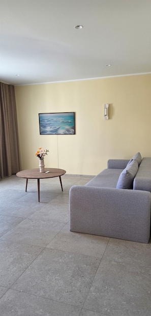 A modern living room with a grey sofa, a round coffee table, and a painting on the wall. - Eldá apartments (Myvatn)