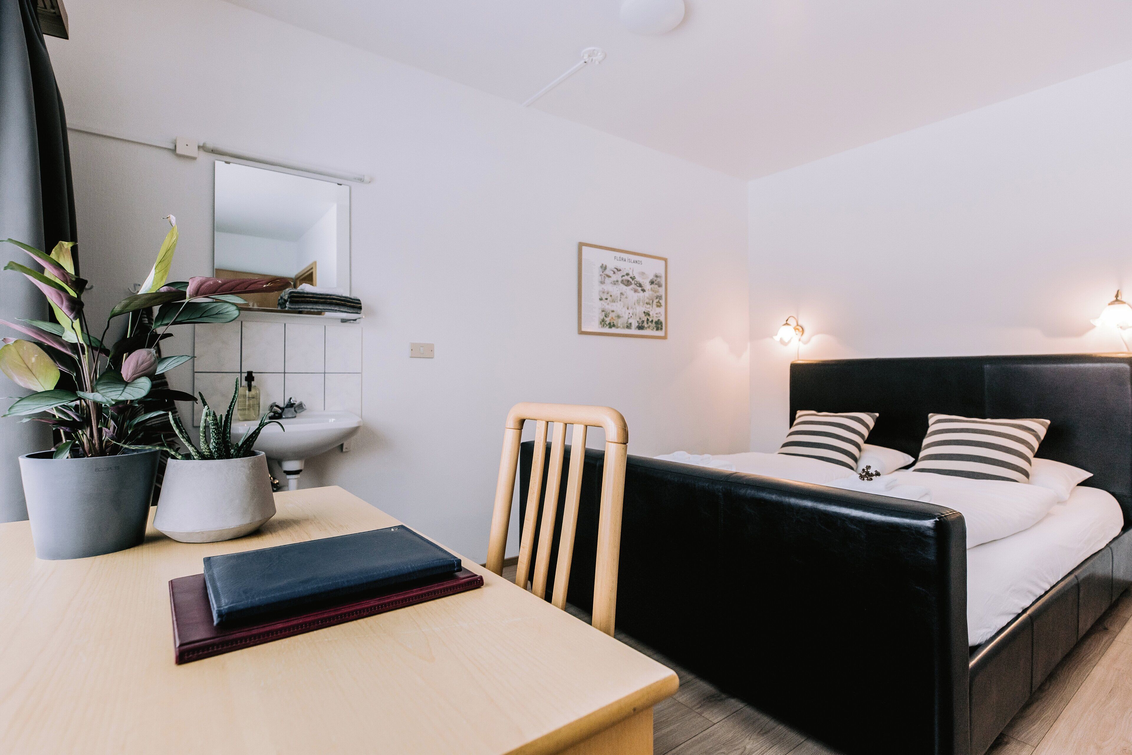 Ein Schlafzimmer mit Bett, Nachttisch, Sessel, Topfpflanzen und einem Wandspiegel.
