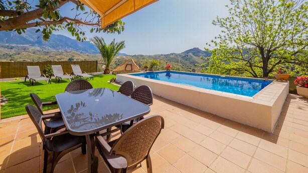Ein Außenpoolbereich mit Tisch und Stühlen, umgeben von einer Terrasse mit Blick auf Hügel.