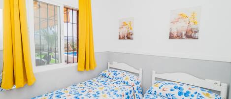 A bedroom with two single beds, a window with yellow curtains, and two wall-mounted pictures.
