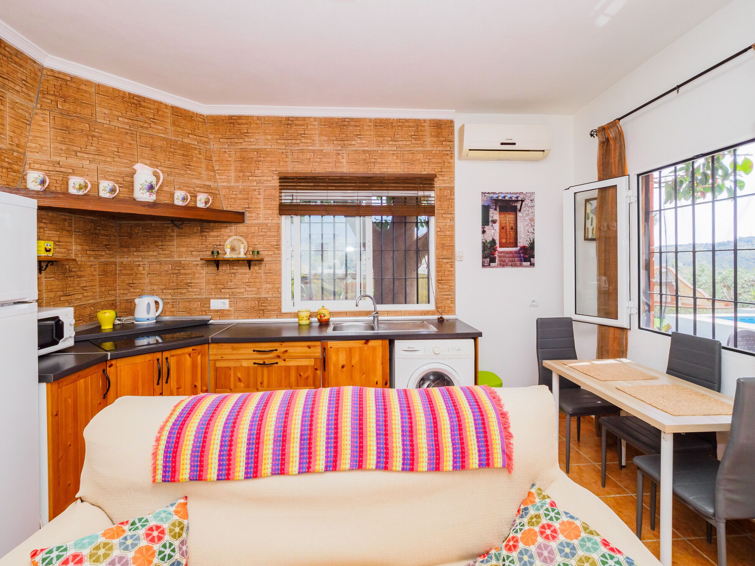 A compact kitchen with a brick backsplash, a window, and a dining area with a table and chairs.