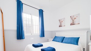 Ein Schlafzimmer mit einem Bett, blauen Vorhängen, weißer Bettwäsche und zwei Wandbildern.