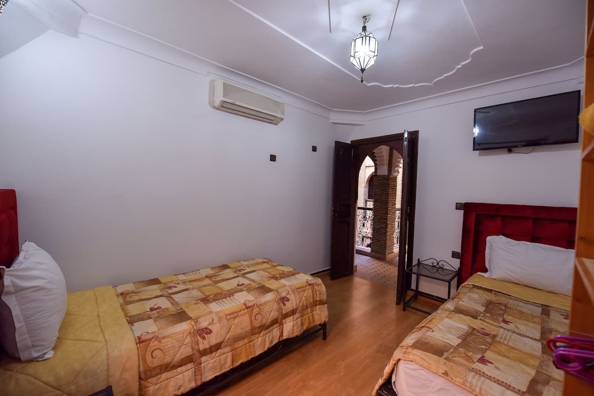A bedroom with two beds, a TV, an air conditioner, and a door leading to a balcony.