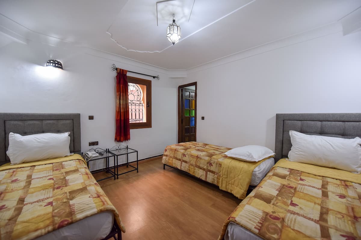A room with two beds, a small table, and a window with a curtain.