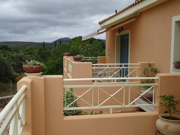 Un balcon avec une balustrade blanche, des plantes en pot et une porte dotée de volets bleus.