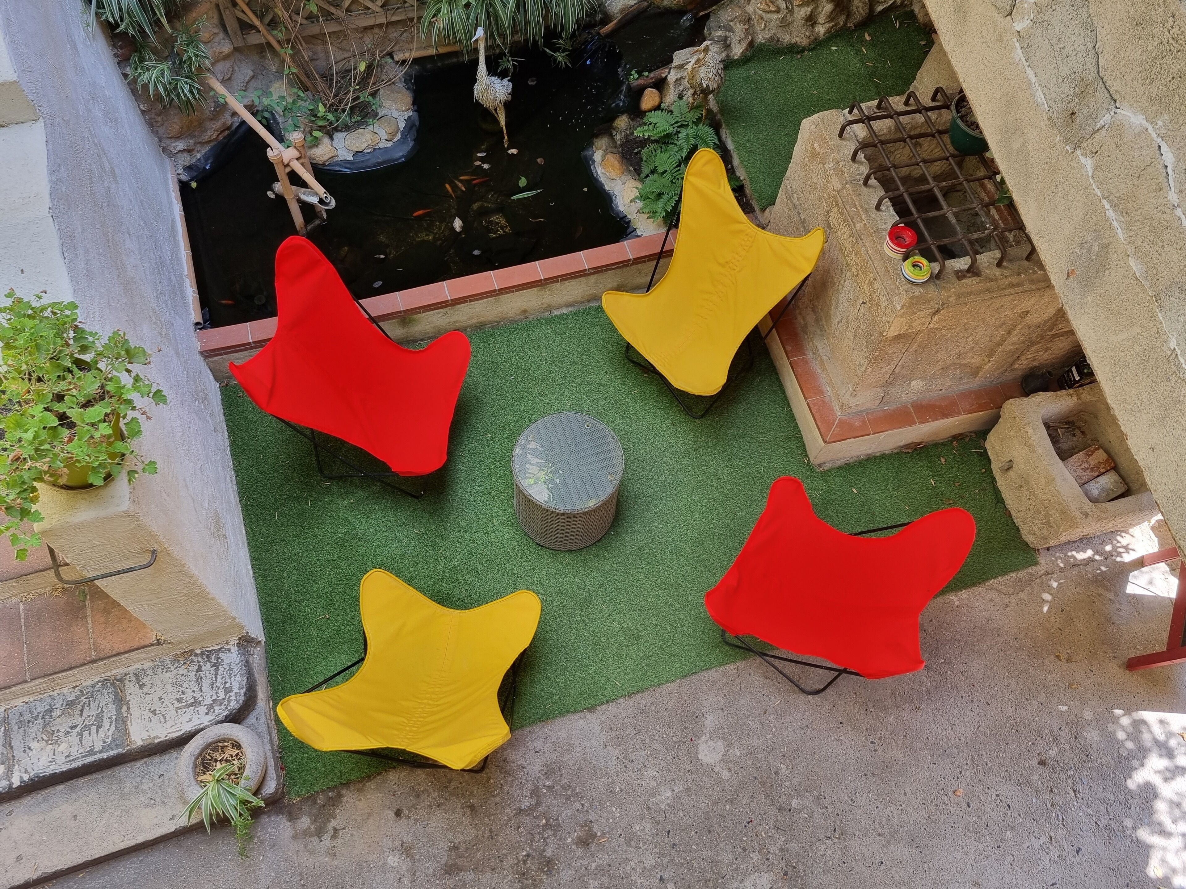 Un jardín en la azotea con un estanque, sillas rojas y amarillas, y una pequeña mesa.