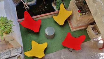 Un jardín en la azotea con un estanque, sillas rojas y amarillas, y una pequeña mesa.