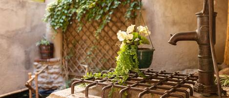A rustic outdoor water feature with a metal spout, a hanging flower pot, and a stone basin.
