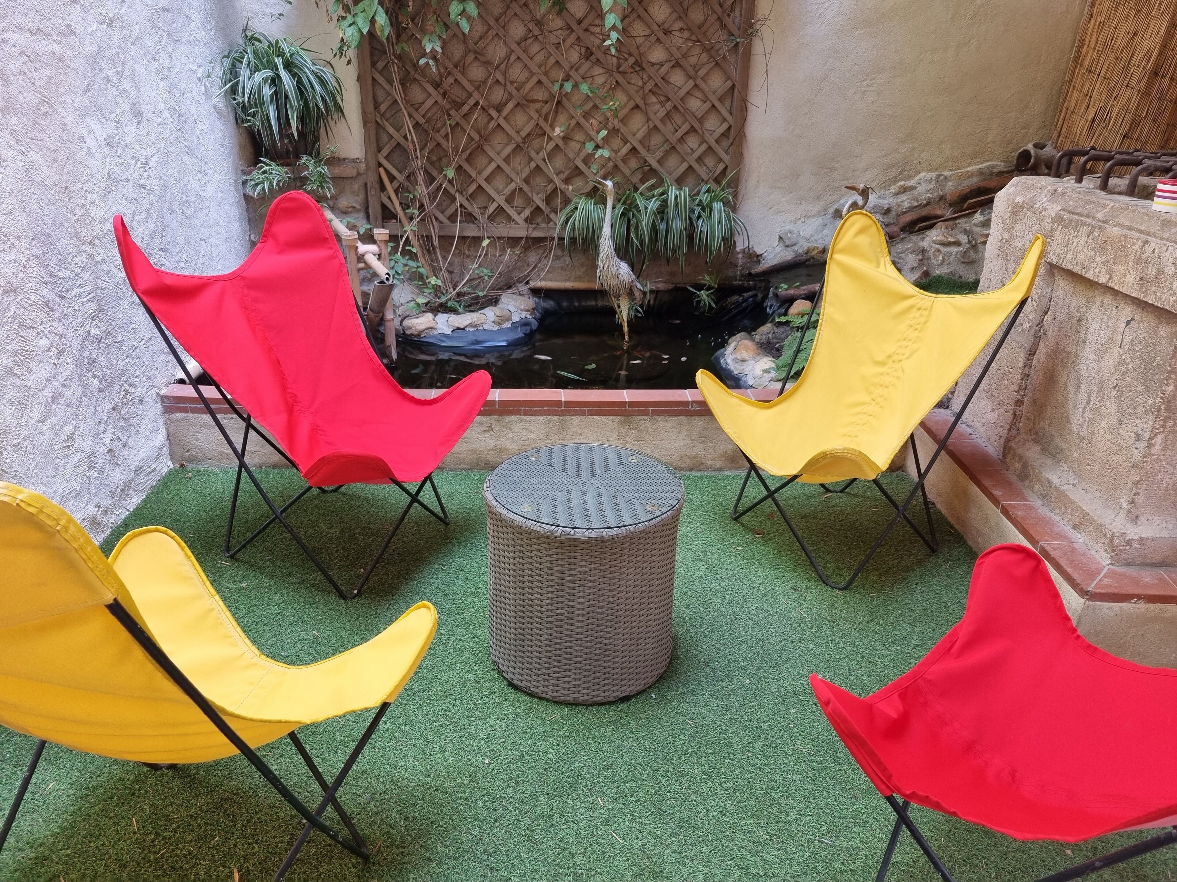 Un espace patio comprenant quatre chaises, une table ronde et un petit bassin avec des plantes.
