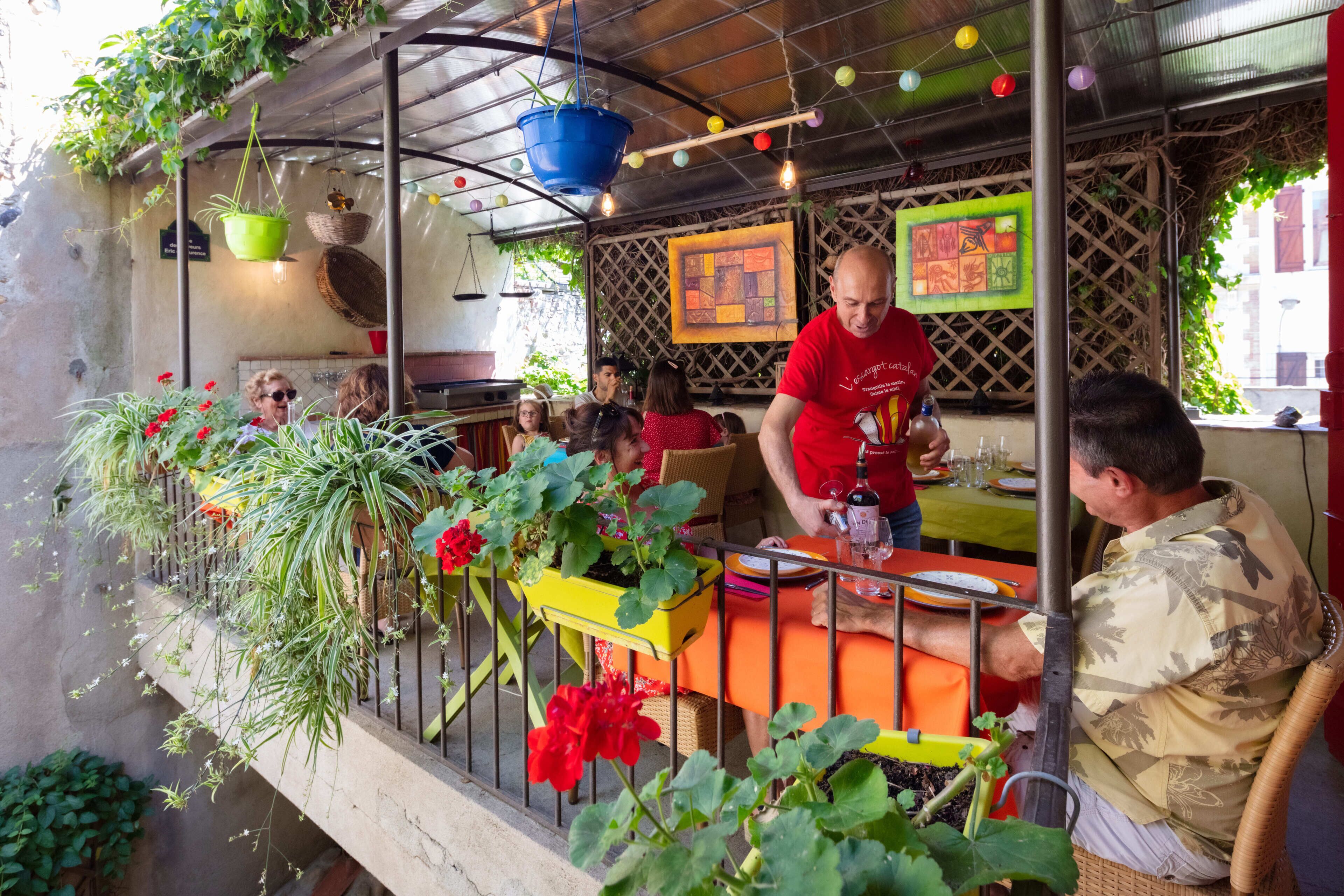 An outdoor dining area with tables and chairs, surrounded by greenery and hanging plants.