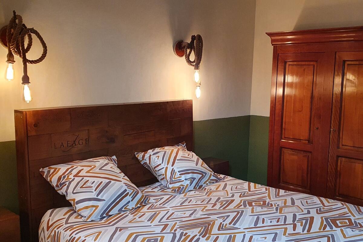 Un lit avec une literie à motifs, une tête de lit en bois et deux appliques murales.