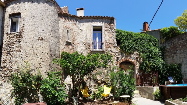 A rustic stone building with a small window and a door. There is a pool with lounge chairs and a table. - La Tour du Terroir (Rivesaltes)