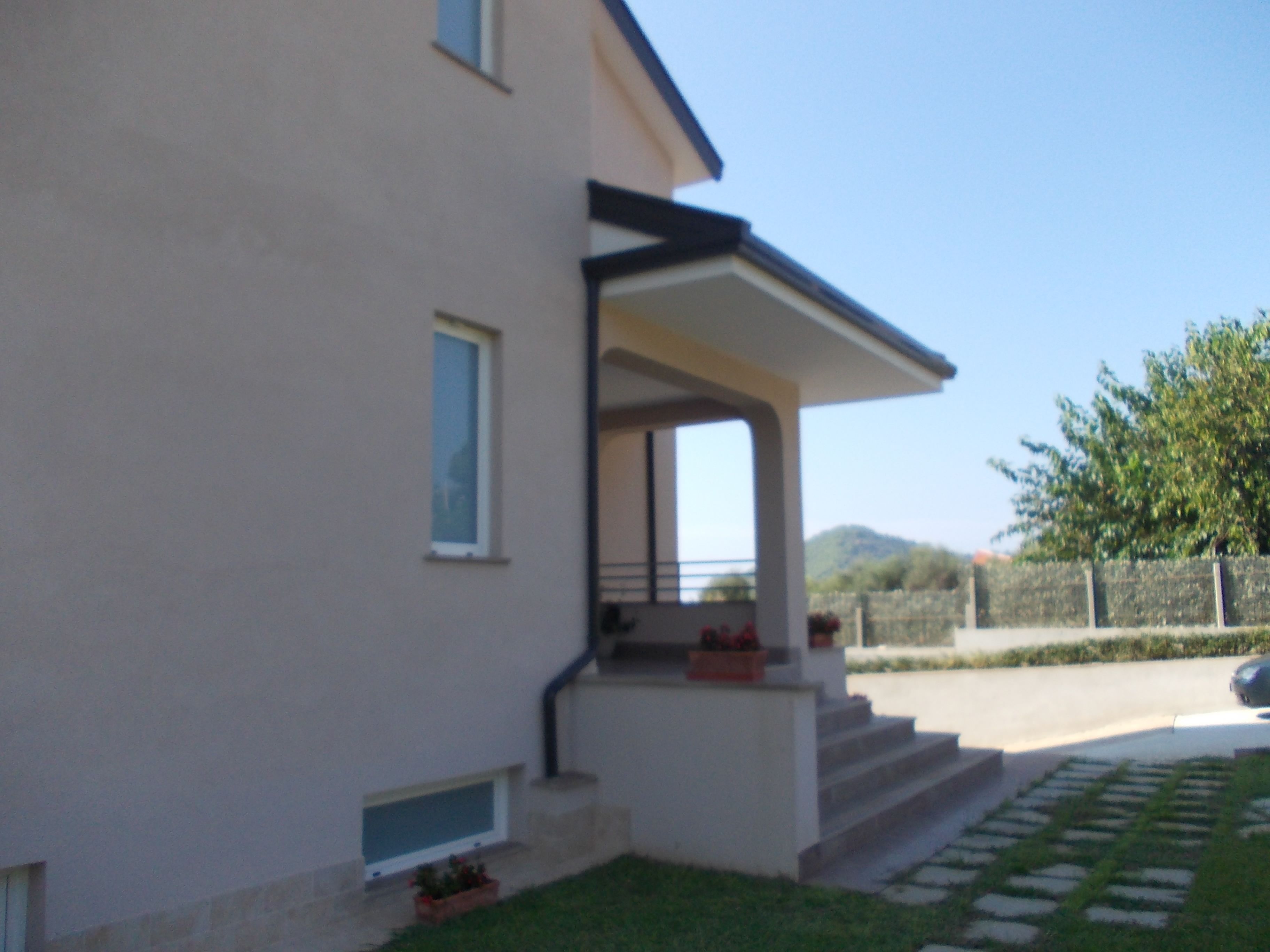 A two-story house with a covered porch, a small garden, and a paved driveway.