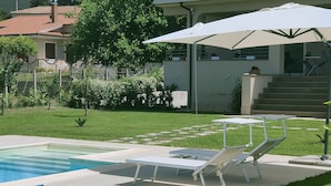 A pool area with lounge chairs and umbrellas, surrounded by a well-maintained lawn and a building with a balcony. - Villa Lauro Luxury B&B (Castellabate)