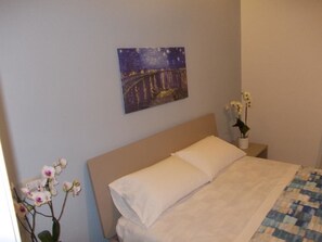 A bedroom with a bed, a night sky painting, and a vase with flowers.