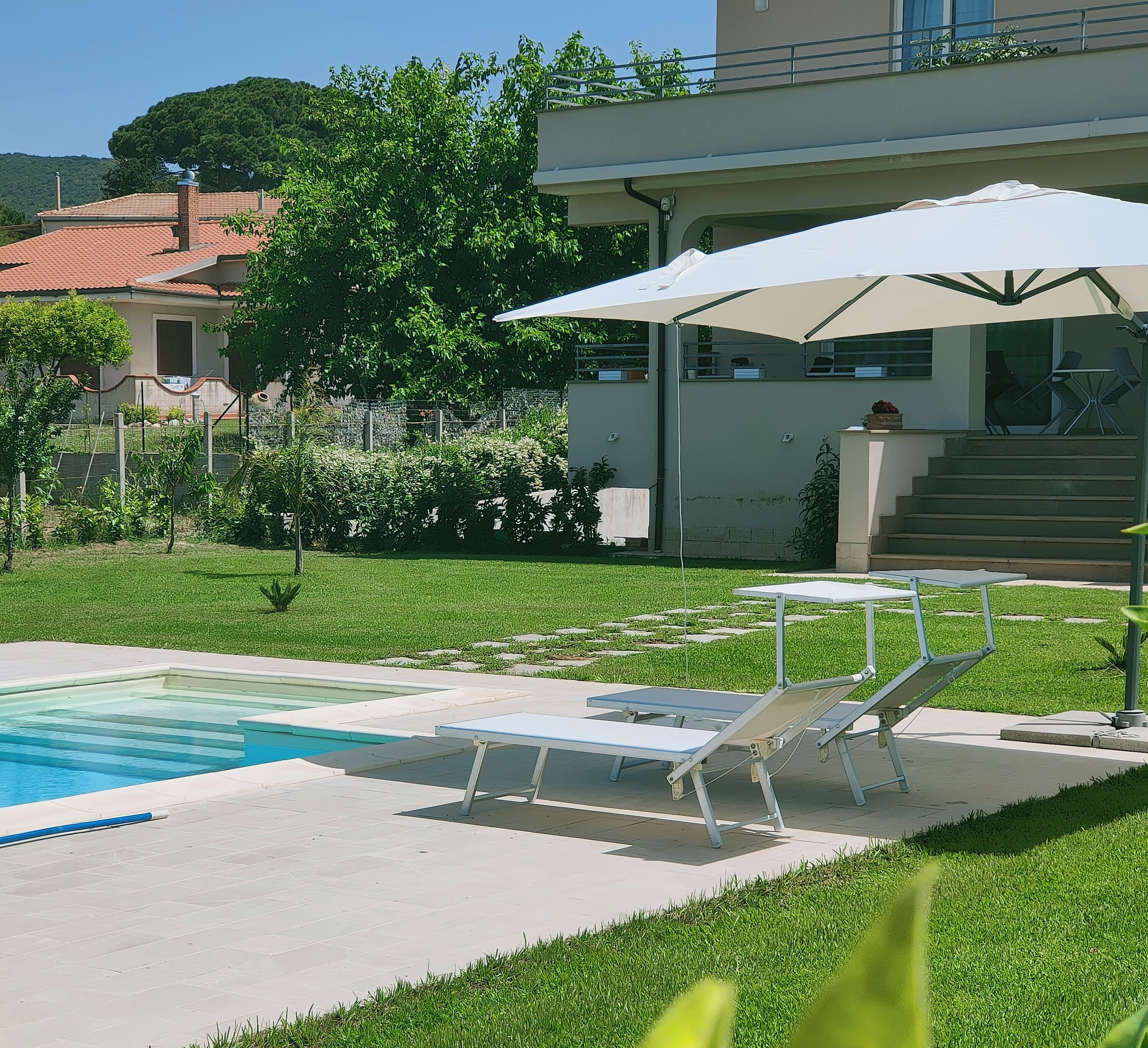 A pool area with lounge chairs and umbrellas, surrounded by a well-maintained lawn and a building with a balcony.