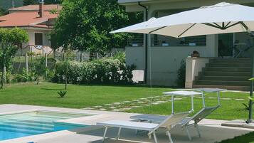 A pool area with lounge chairs and umbrellas, surrounded by a well-maintained lawn and a building with a balcony.