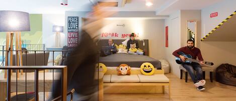 A modern hotel room with a bed, a sofa, a desk, and a guitar.