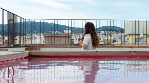 A person standing on a balcony with a view of a cityscape and mountains in the distance. - Yeah Barcelona Hostel (Barcelona)