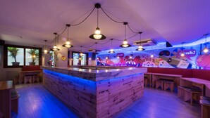 A modern bar area with wooden bar counters, hanging pendant lights, and a colorful mural on the wall. - Yeah Barcelona Hostel (Barcelona)