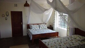 Een slaapkamer met een bed, een nachtkastje, een raam met gordijnen, een deur en een wandairconditioning.
