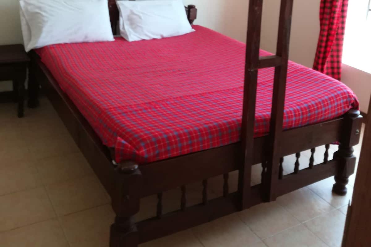 Una cama individual con dosel, una colcha roja a cuadros y almohadas blancas.