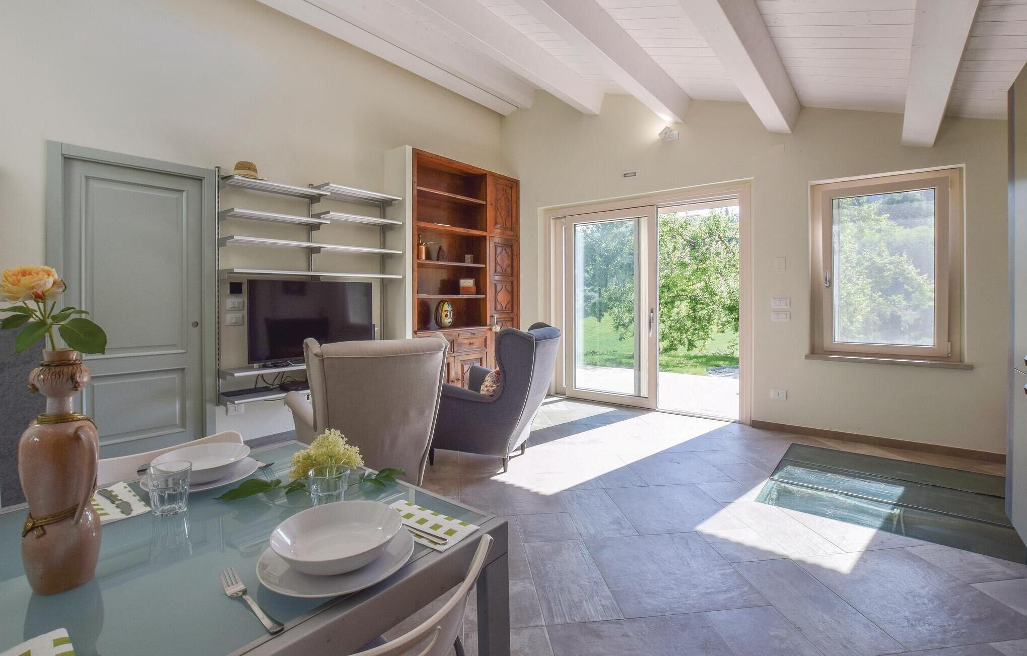 A dining area with a glass table, chairs, a vase with flowers, a television, and a sliding glass door leading to a garden.