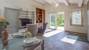 Un coin repas avec une table en verre, des chaises, un vase avec des fleurs, un téléviseur et une porte-fenêtre coulissante donnant sur un jardin.