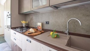 Une cuisine moderne équipée d’un four encastré, d’une cuisinière à gaz, d’un évier en acier inoxydable et d’une planche à découper en bois.