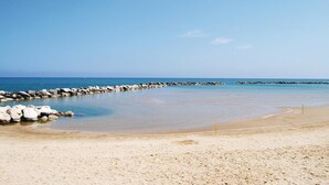 Une plage avec une eau d’un bleu limpide, un rivage sablonneux et une digue rocheuse.