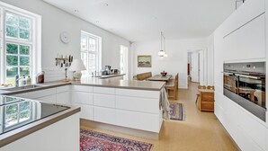 Ett modernt kök med vita skåp, en stor köksö och en inbyggd ugn.