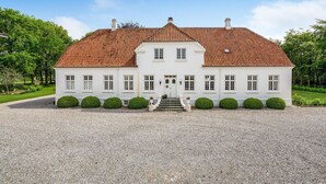 En stor, vit byggnad med ett rött tegeltak, många fönster och en grusuppfart.