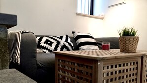 A living room with a grey sofa, black and white patterned pillows, a woven basket with a plant, and a small wooden table with a glass of red drink. - Old Jaffa Designers House (Tel Aviv)