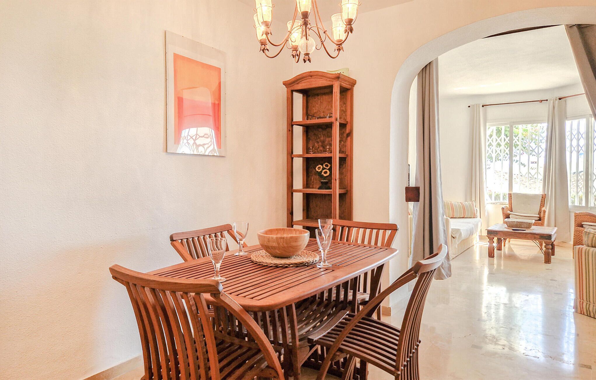 Un'area pranzo con un tavolo e sedie in legno, un lampadario e un armadietto con scaffali.
