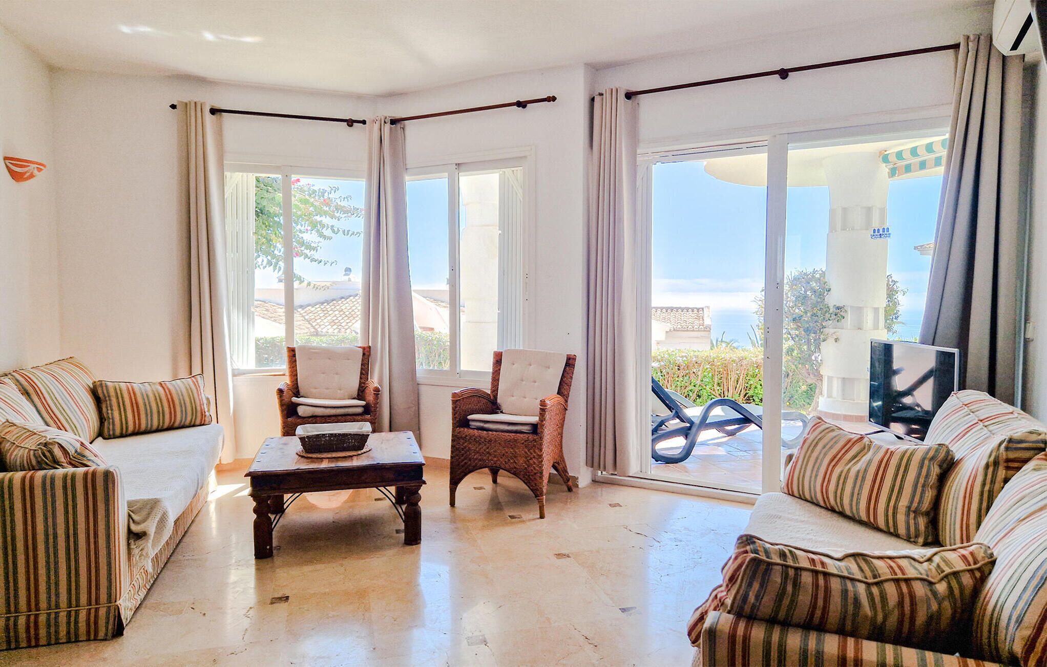 A spacious living room with a large window, a sofa, two armchairs, and a coffee table.