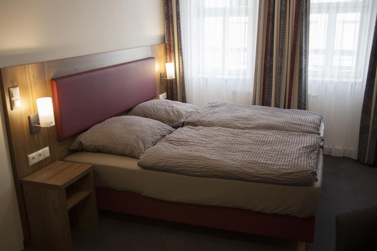 A double bed with a headboard, bedside tables, and a window with curtains.