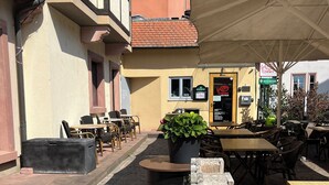 En udendørs café med borde, stole, en skraldespand og en potteplante.